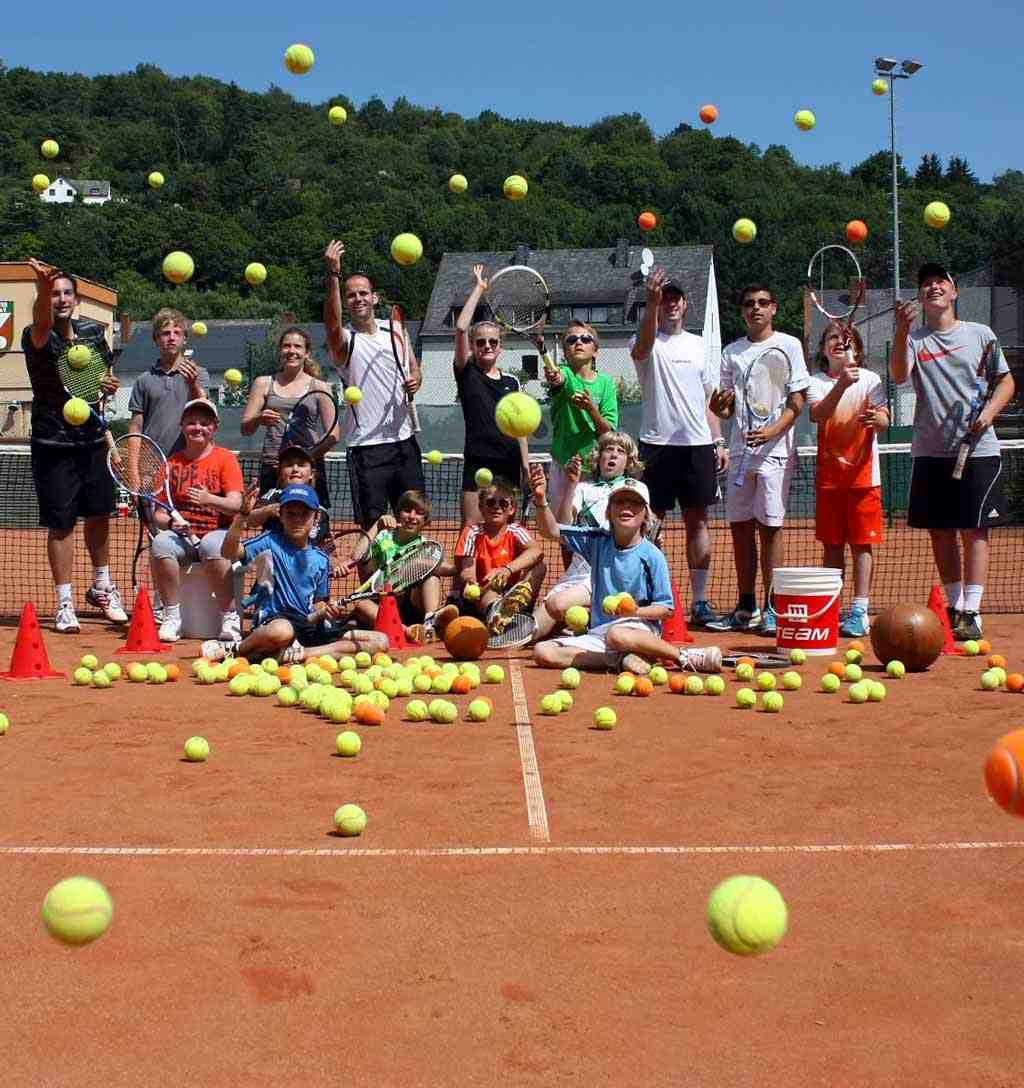 Mehrere fröhliche Kinder und Jugendliche auf einem Tennisplatz werfen Tennisbälle in Richtung Betrachter
